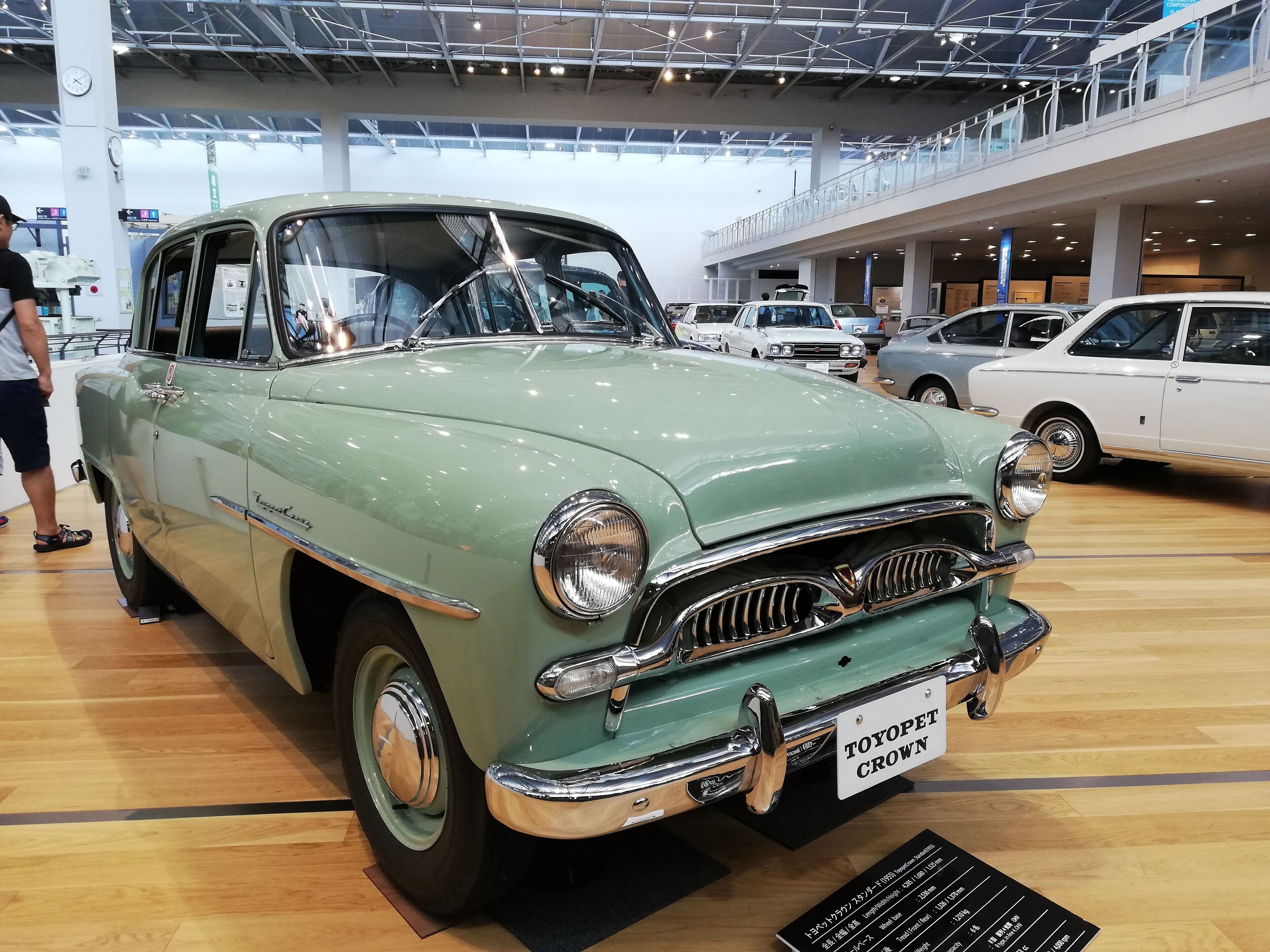A vintage car on display in a spacious, modern indoor setting with high ceilings and a wooden floor.