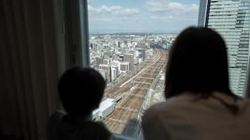 Due persone che guardano attraverso una finestra su un panorama urbano con edifici e binari ferroviari.