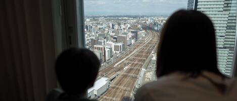 Two people looking out of a window at a cityscape with buildings and train tracks.