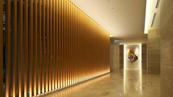 Un pasillo moderno con listones verticales de madera y suelo pulido, que conduce a una zona de recepción con un logotipo en la pared.