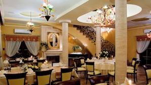 Comedor con varias mesas dispuestas para una comida, una escalera y una chimenea.