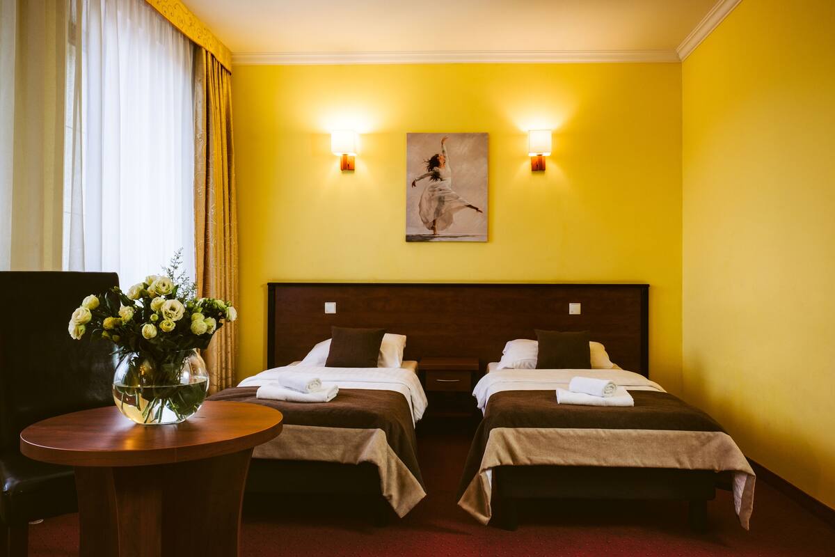 Une chambre d’hôtel avec deux lits, un tableau au mur et un vase rempli de fleurs sur une table.