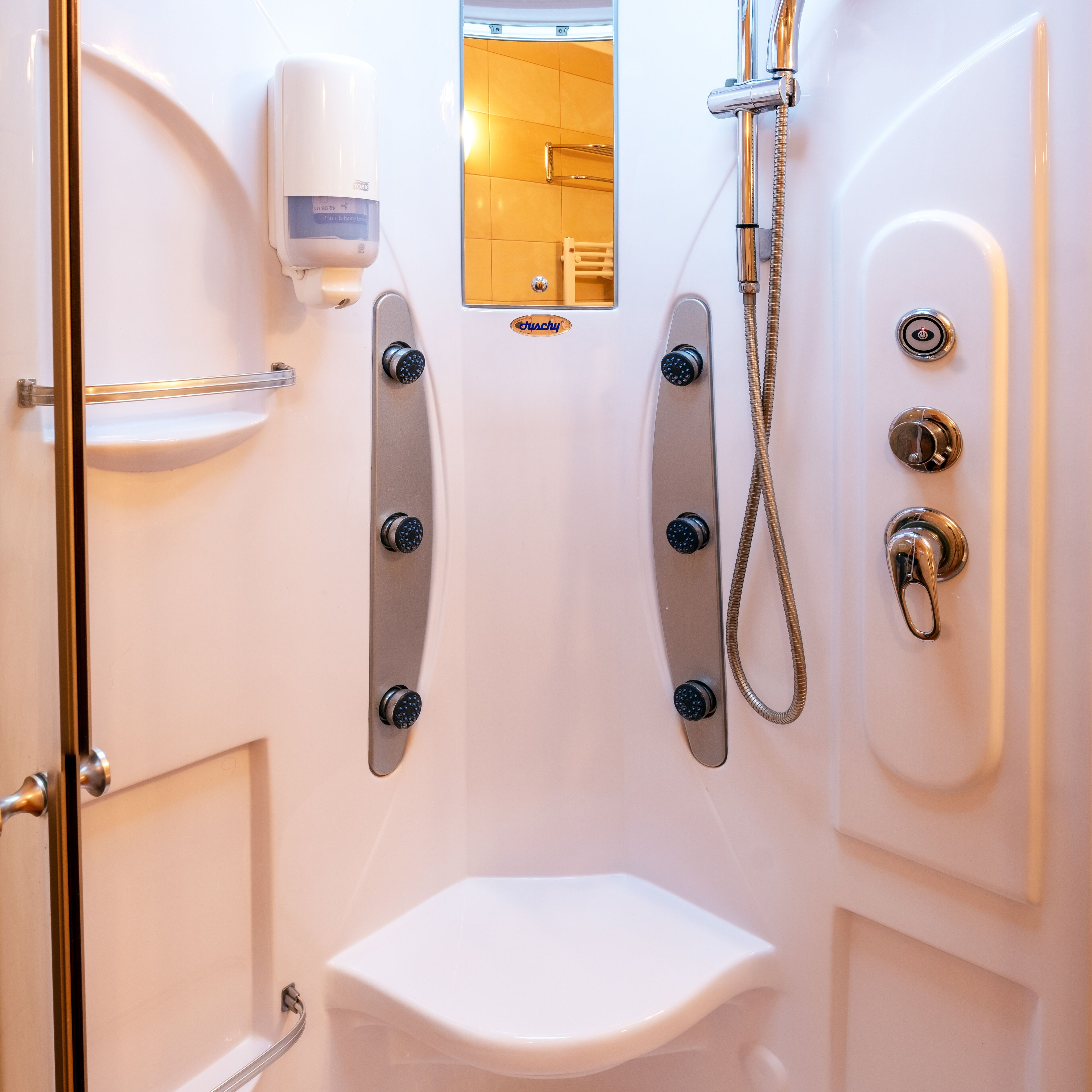 Un baño moderno con inodoro, ducha con cabezal de ducha manual y dispensador de jabón.