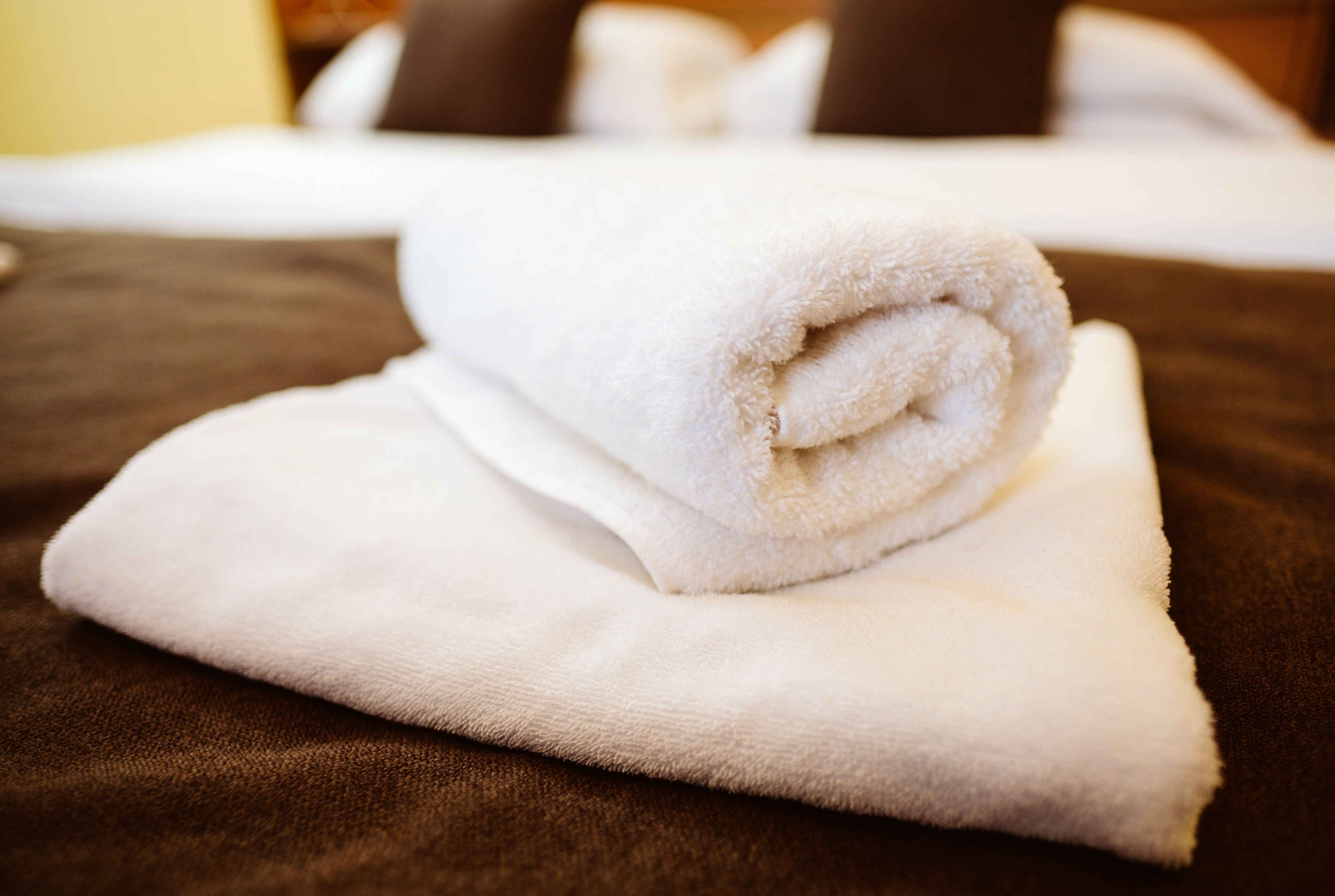A neatly folded white towel on a brown bedspread.