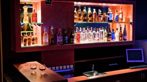 Zona de bar con estantes de botellas de licor, un piano y un monitor de computadora.