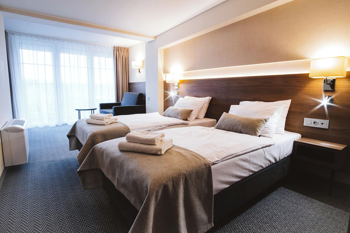 Une chambre d’hôtel avec deux lits, un coin salon et une grande fenêtre avec des rideaux.