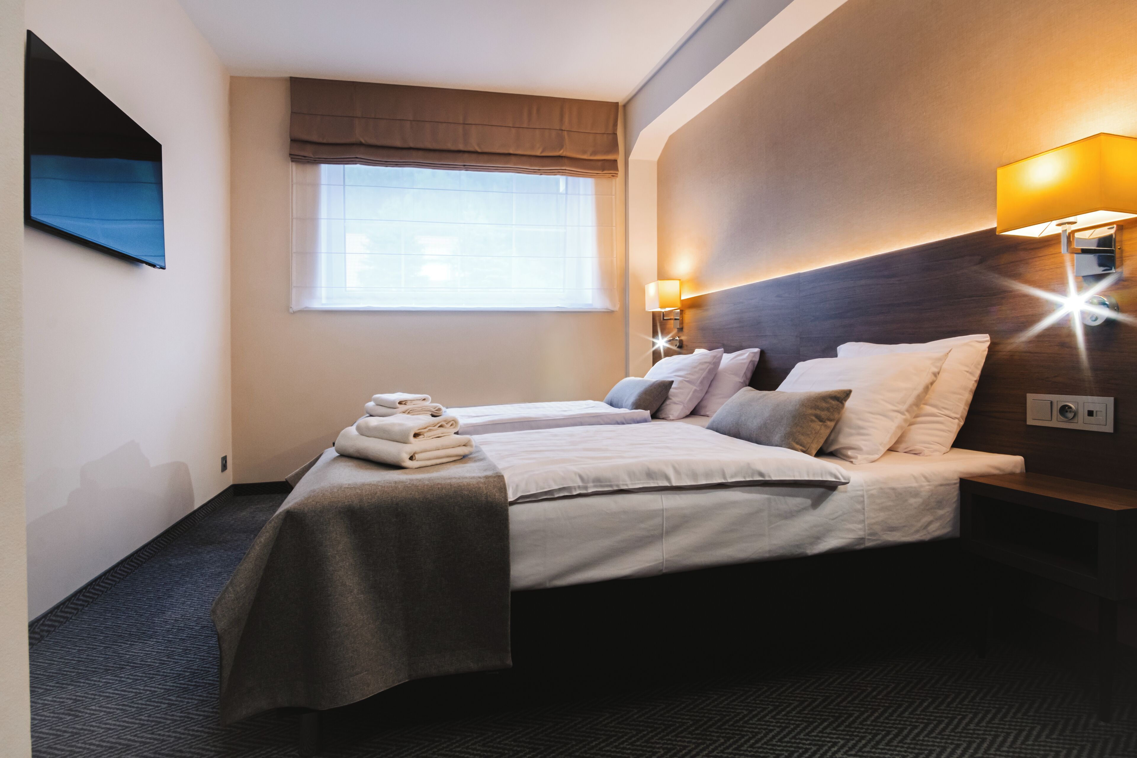 Hotelkamer met twee bedden, een groot raam met uitzicht, een wandtelevisie en een bedlamp.