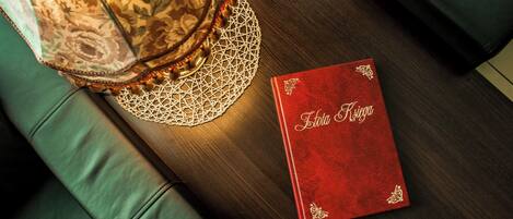 A red book titled "Lotta Reyes" on a wooden table next to a green couch and a decorative lamp.