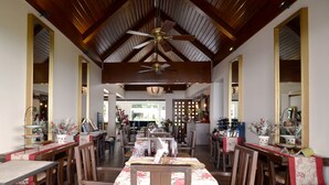 Un vaste espace dédié à la salle à manger, avec des tables et des chaises en bois, un ventilateur de plafond et de grands miroirs sur les murs.