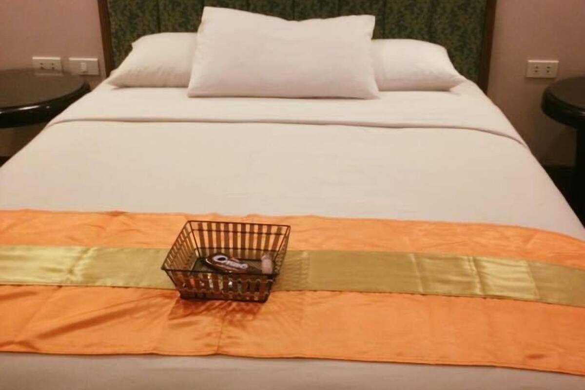 A hotel room with a neatly made bed, a headboard with a patterned design, and a small bedside table with a lamp.