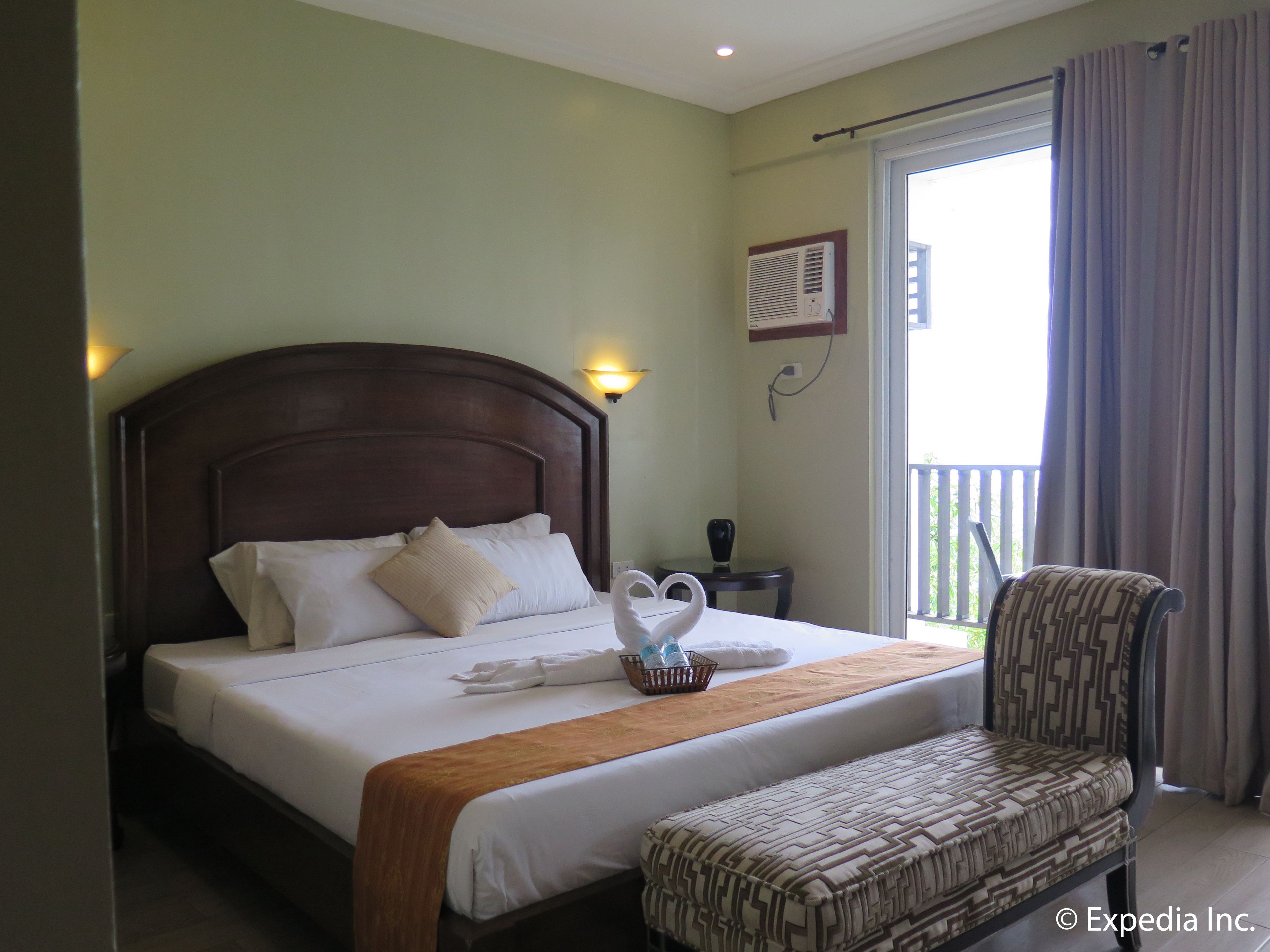 Habitación de hotel con una cama grande, una mesita de noche, una silla, una ventana con cortinas y un aire acondicionado instalado en la pared.