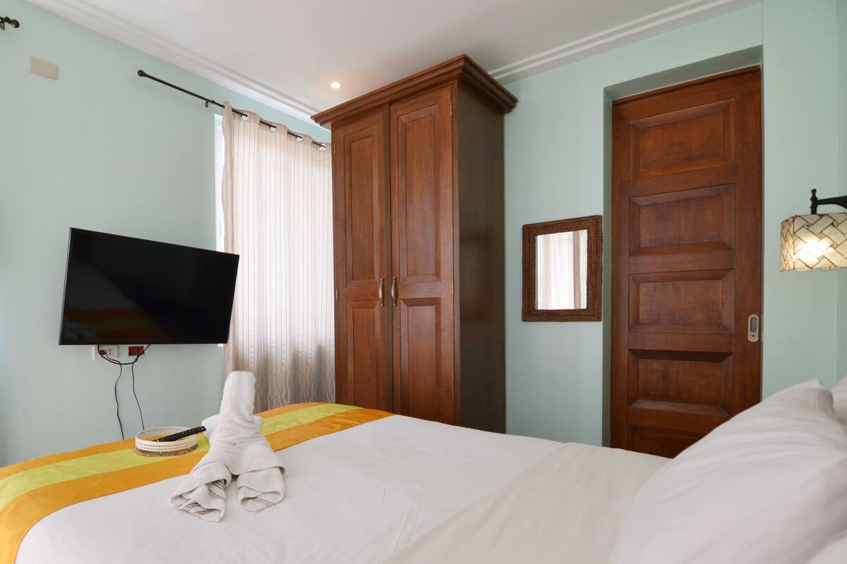 A hotel room with a bed, a television mounted on the wall, a wardrobe, and a bedside lamp.