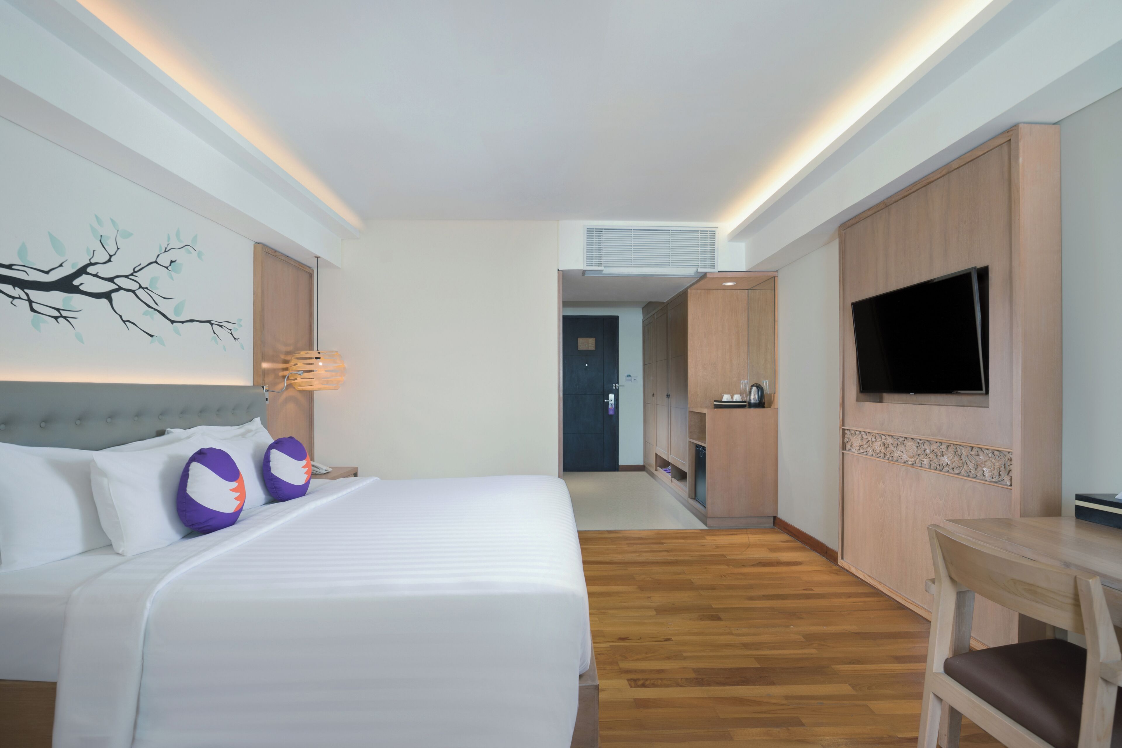 A hotel room with a bed, a TV, a desk, and a wall-mounted artwork.