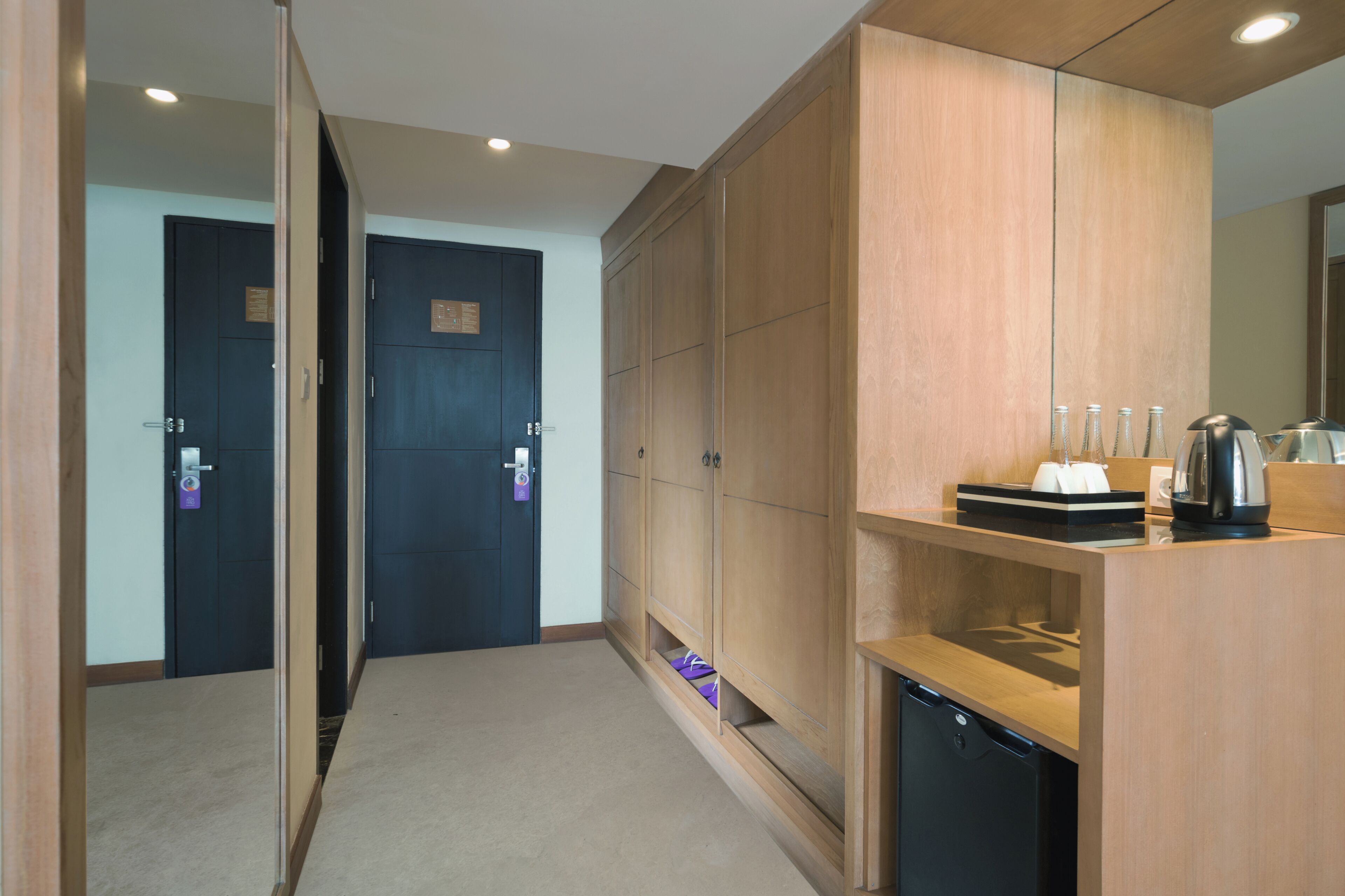 A hotel room with a wooden wardrobe, a small kitchen area with a coffee maker, and a door with a keycard lock.