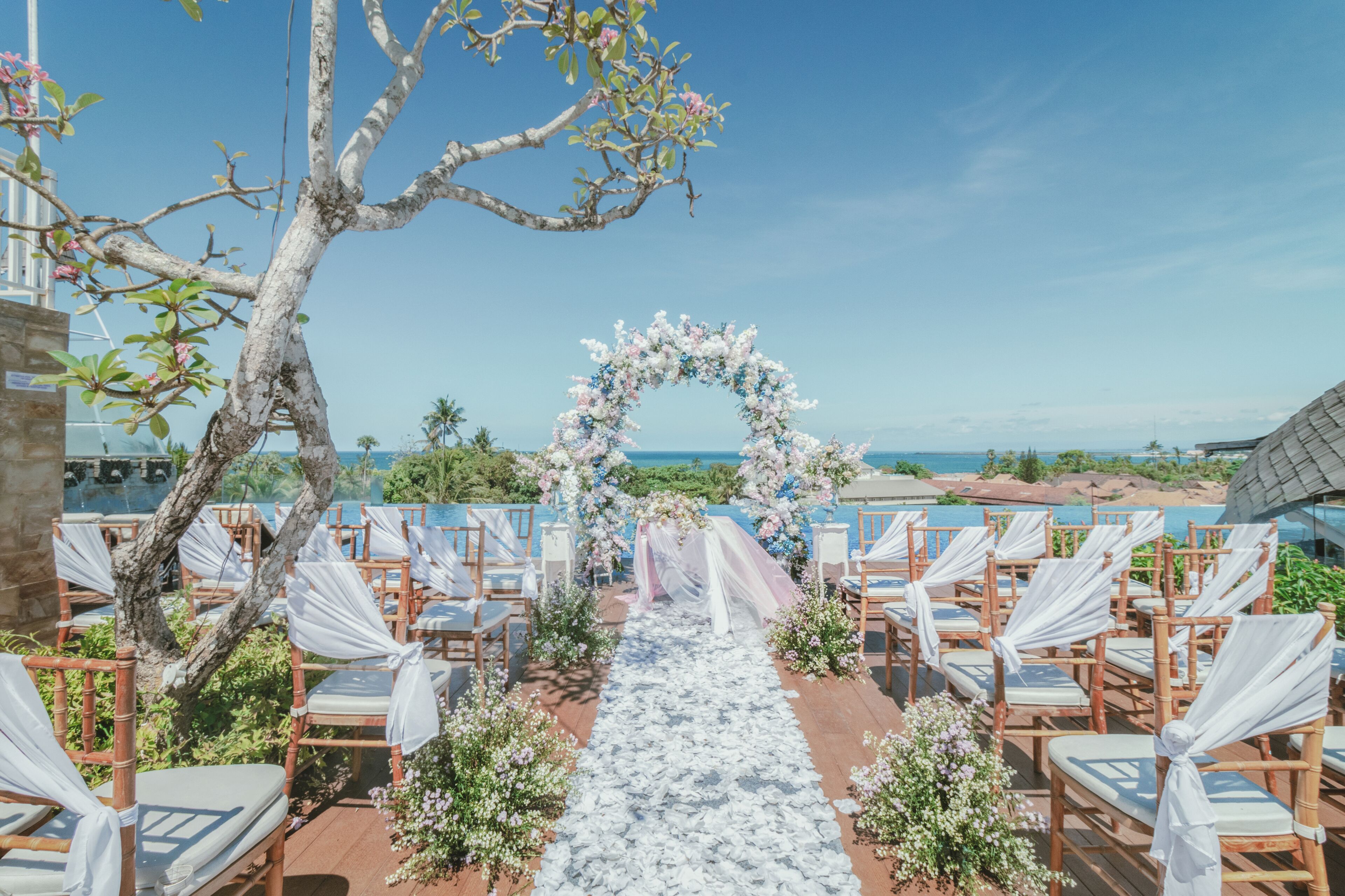 Pasillo nupcial al aire libre con sillas y un arco floral, con vistas a una playa.