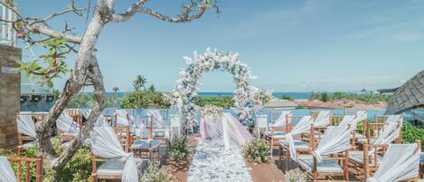 Pasillo nupcial al aire libre con sillas y un arco floral, con vistas a una playa.