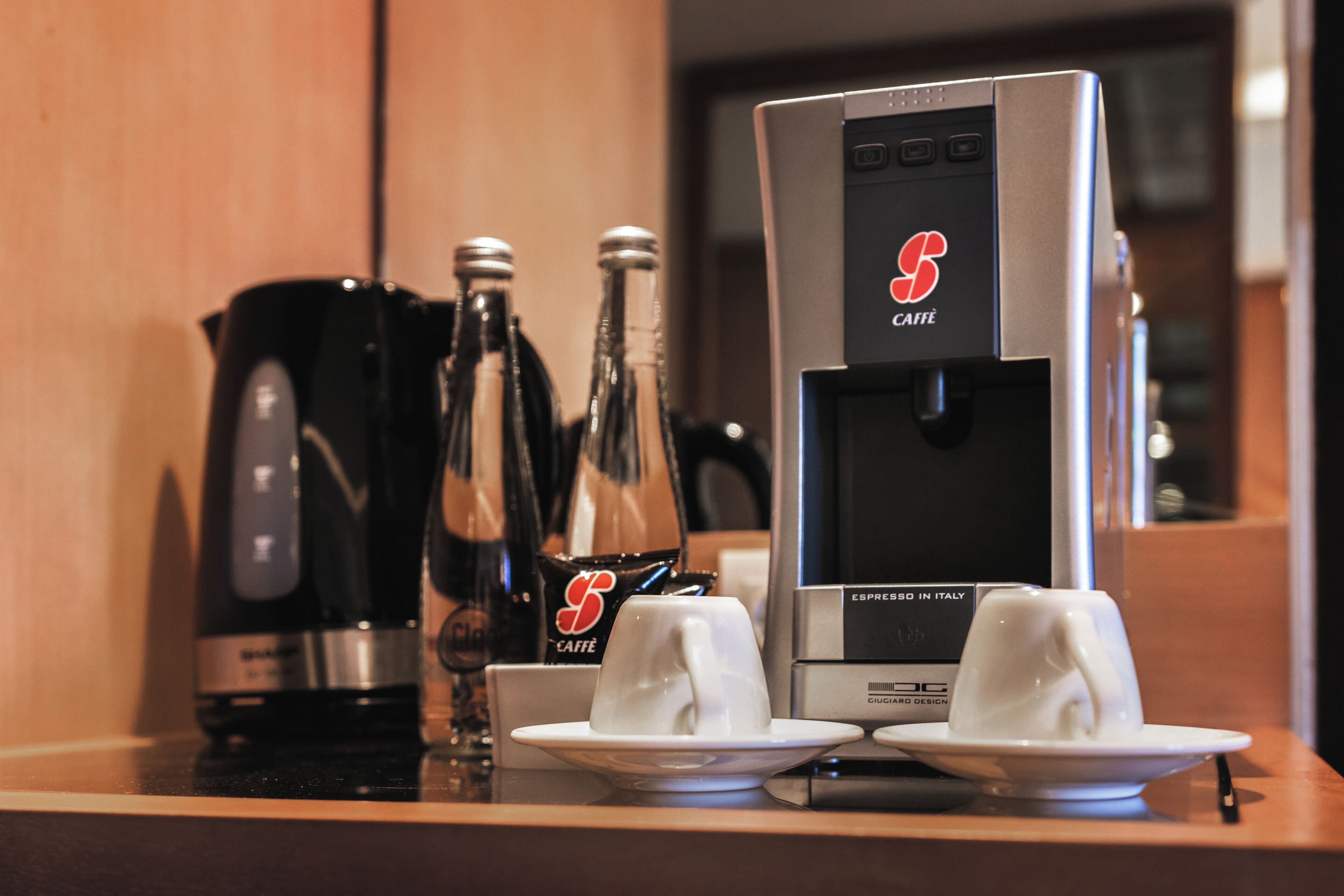 A coffee machine with a branded logo, two bottles of water, and two cups on a table.