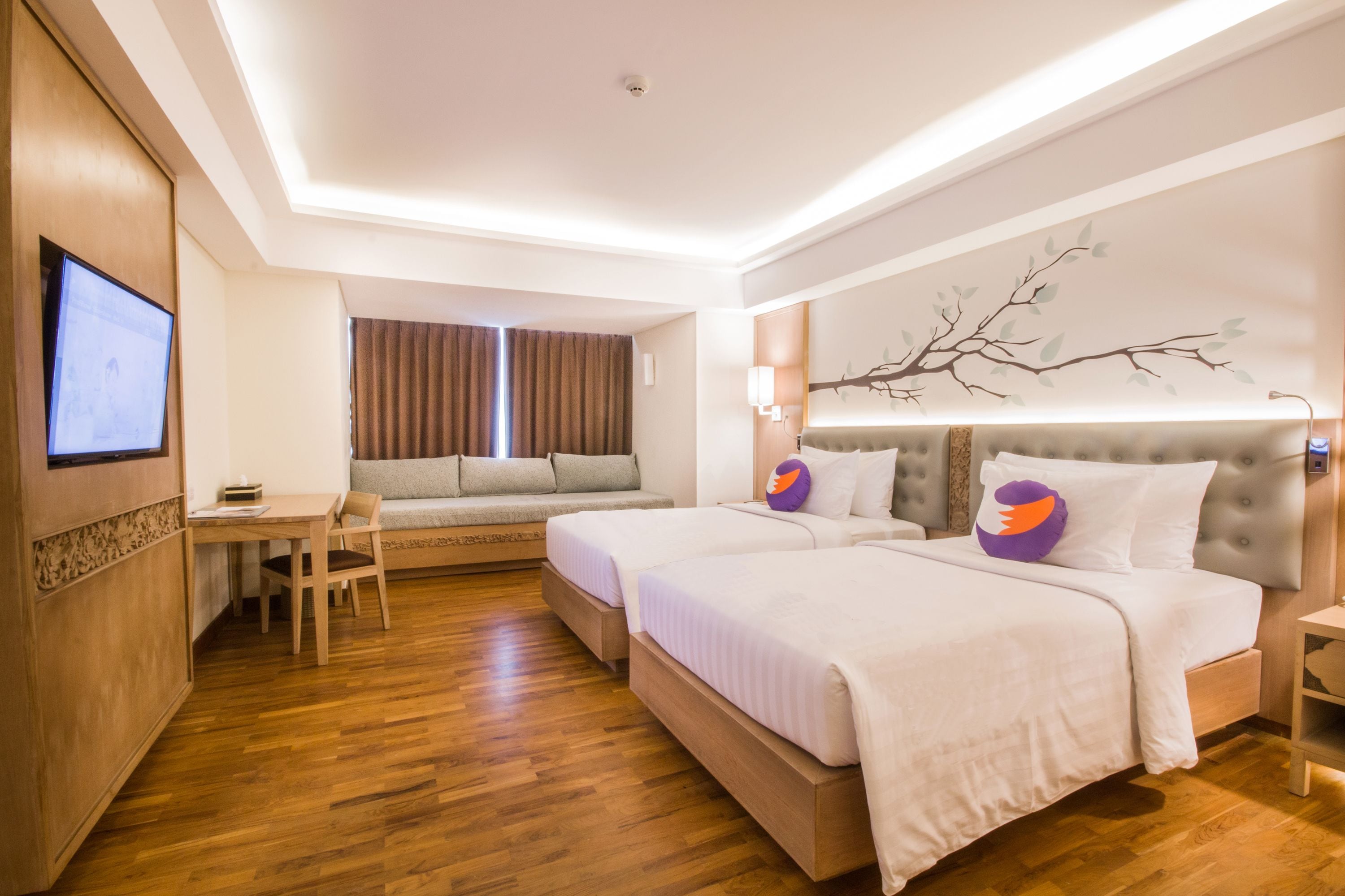 A hotel room with two beds, a desk, a sofa, and a TV.