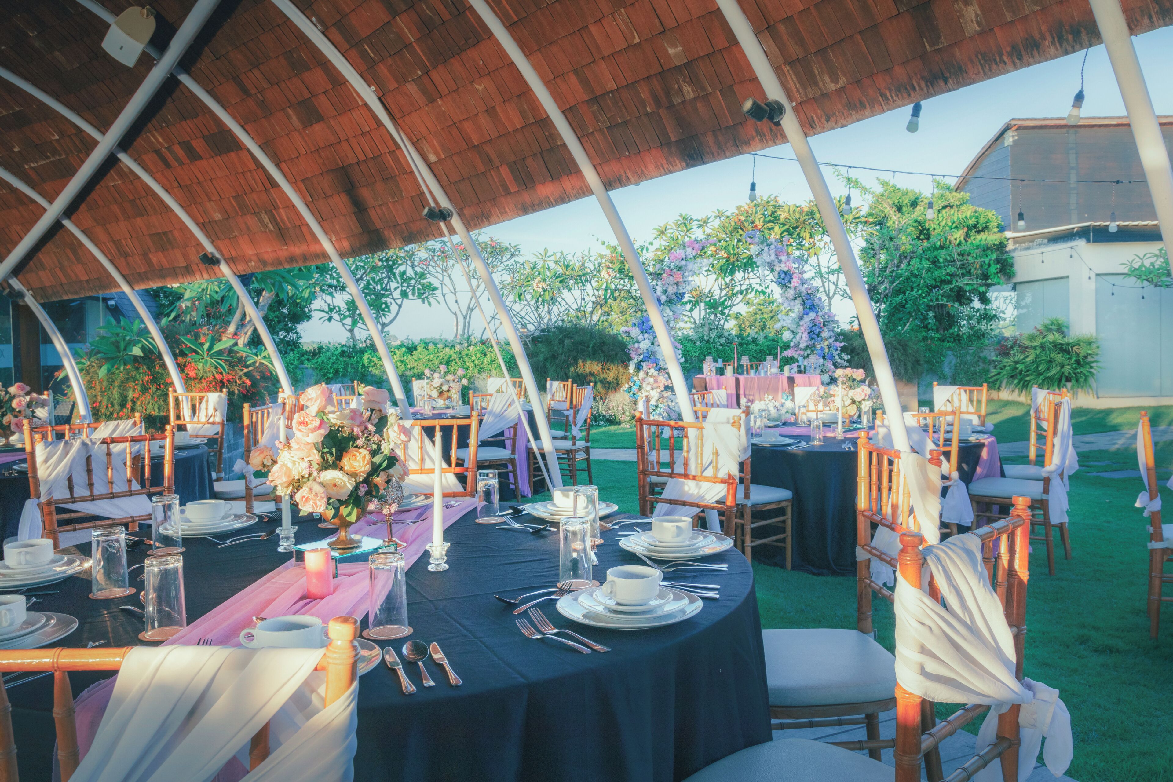 Un área de comedor al aire libre con mesas redondas, sillas y una estructura de techo de paja.
