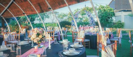 Un área de comedor al aire libre con mesas redondas, sillas y una estructura de techo de paja.