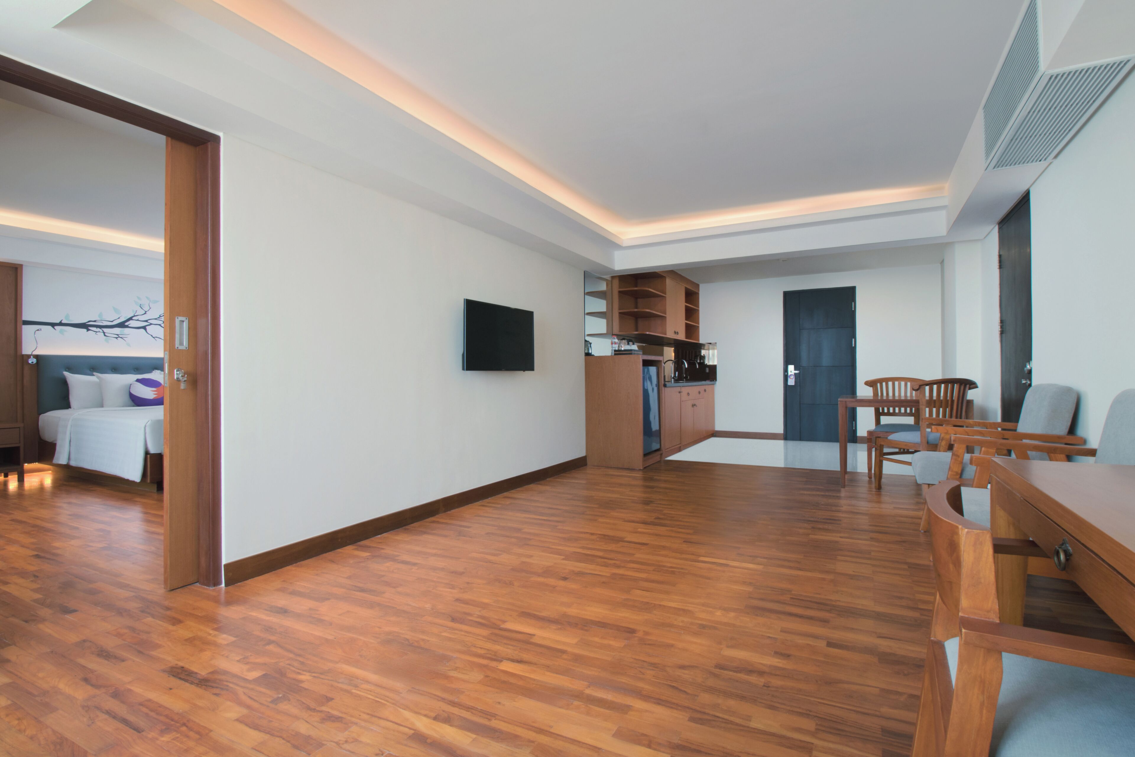 Un'ampia zona giorno con pavimento in legno, un tavolo da pranzo con sedie, un angolo cottura con mobili e un televisore fissato al muro.
