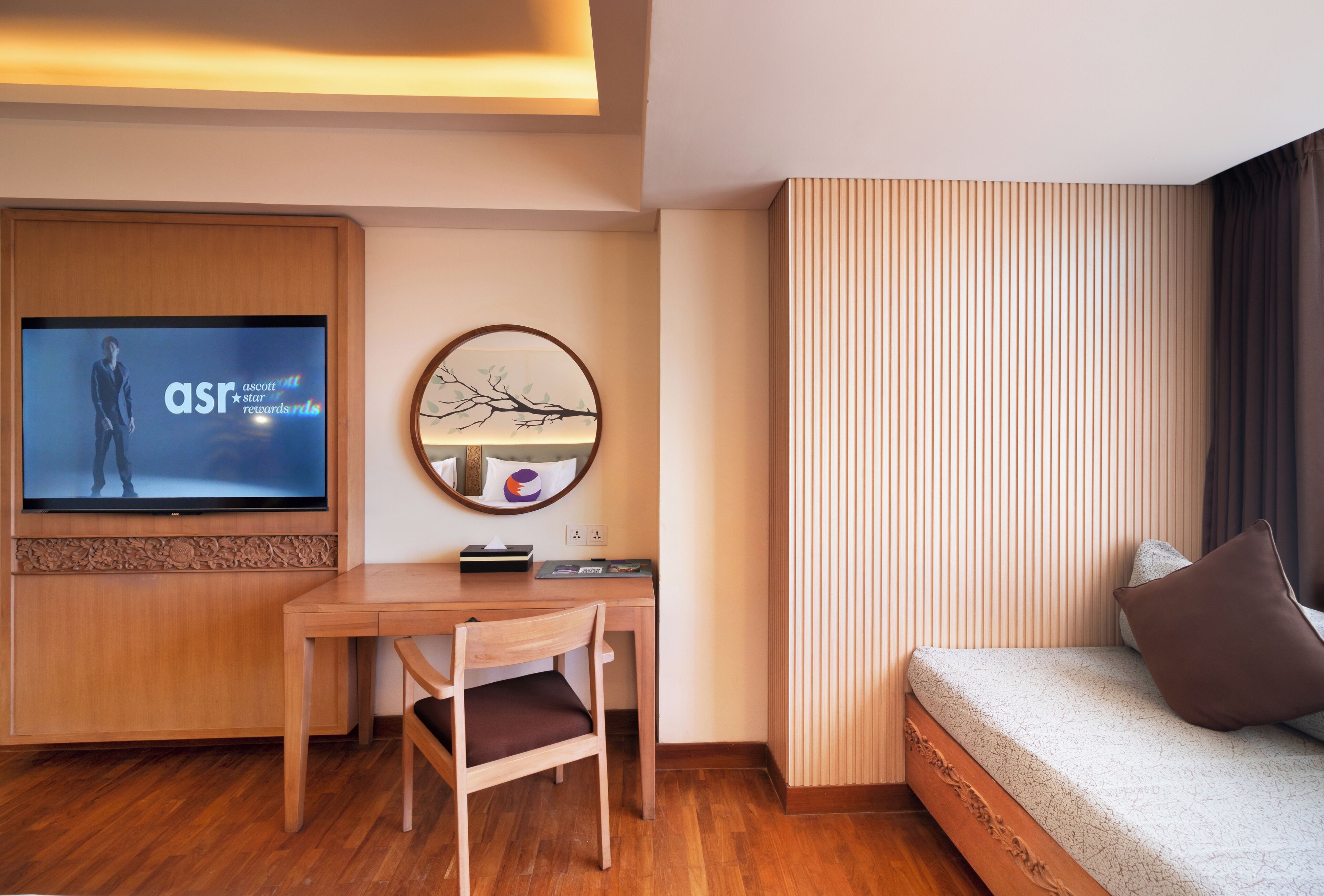 Ein Hotelzimmer mit einem Holztisch, einem Fernseher, einer runden Wanduhr und einem Bett mit Kissen.
