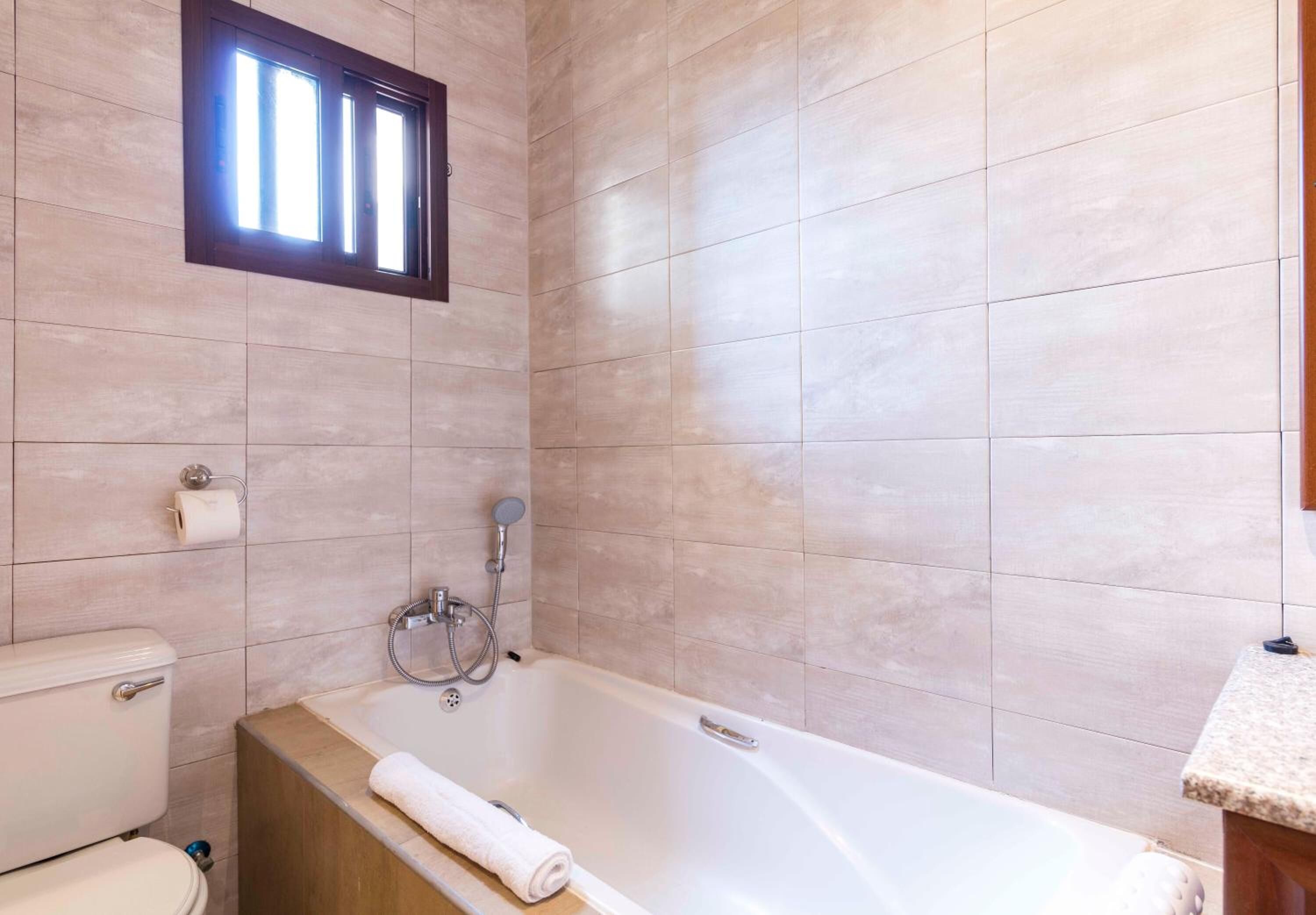 A bathroom with a bathtub, toilet, and a window.