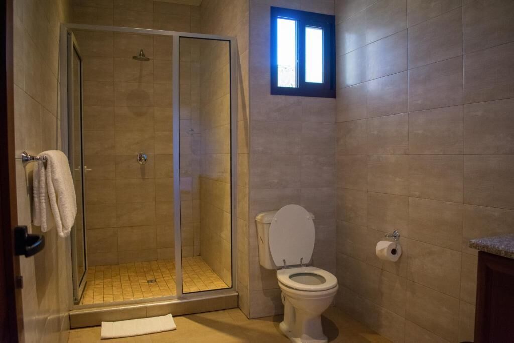 Een badkamer met een douchecabine van glas, een toilet en een klein raam.