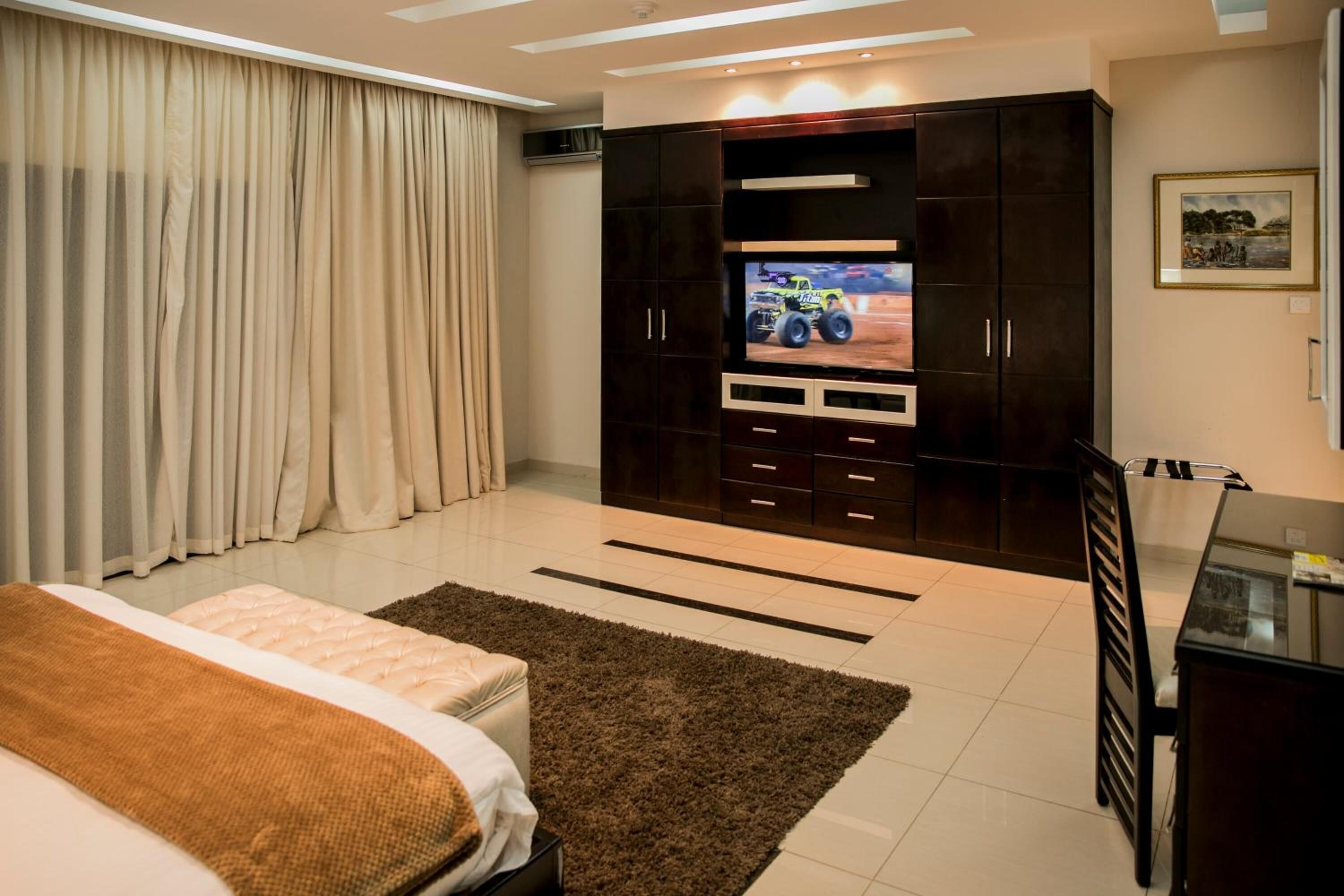 A modern bedroom with a large TV, dark wooden wardrobe, and a bed with a brown blanket.