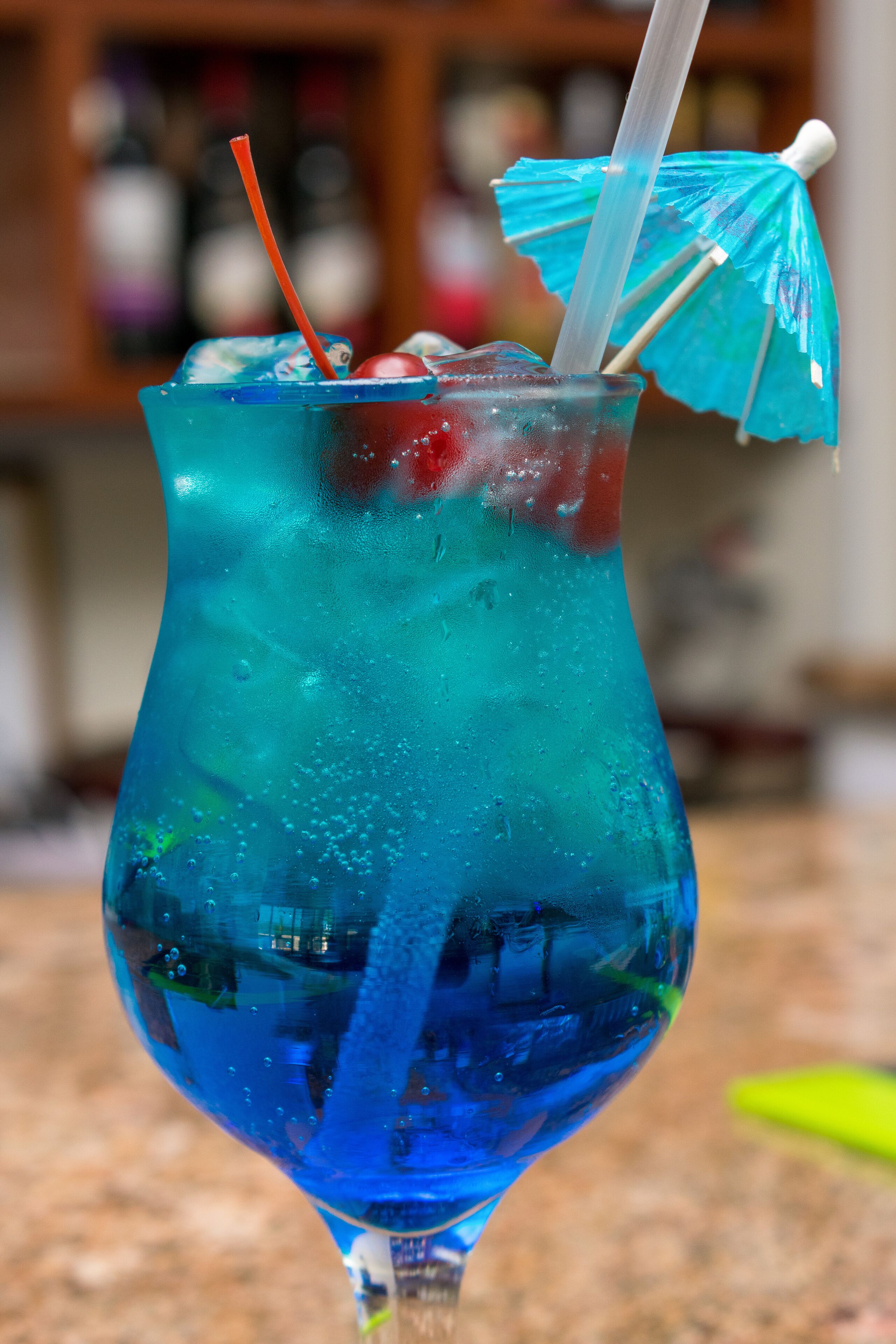 A cocktail in a glass with a straw and a blue umbrella.