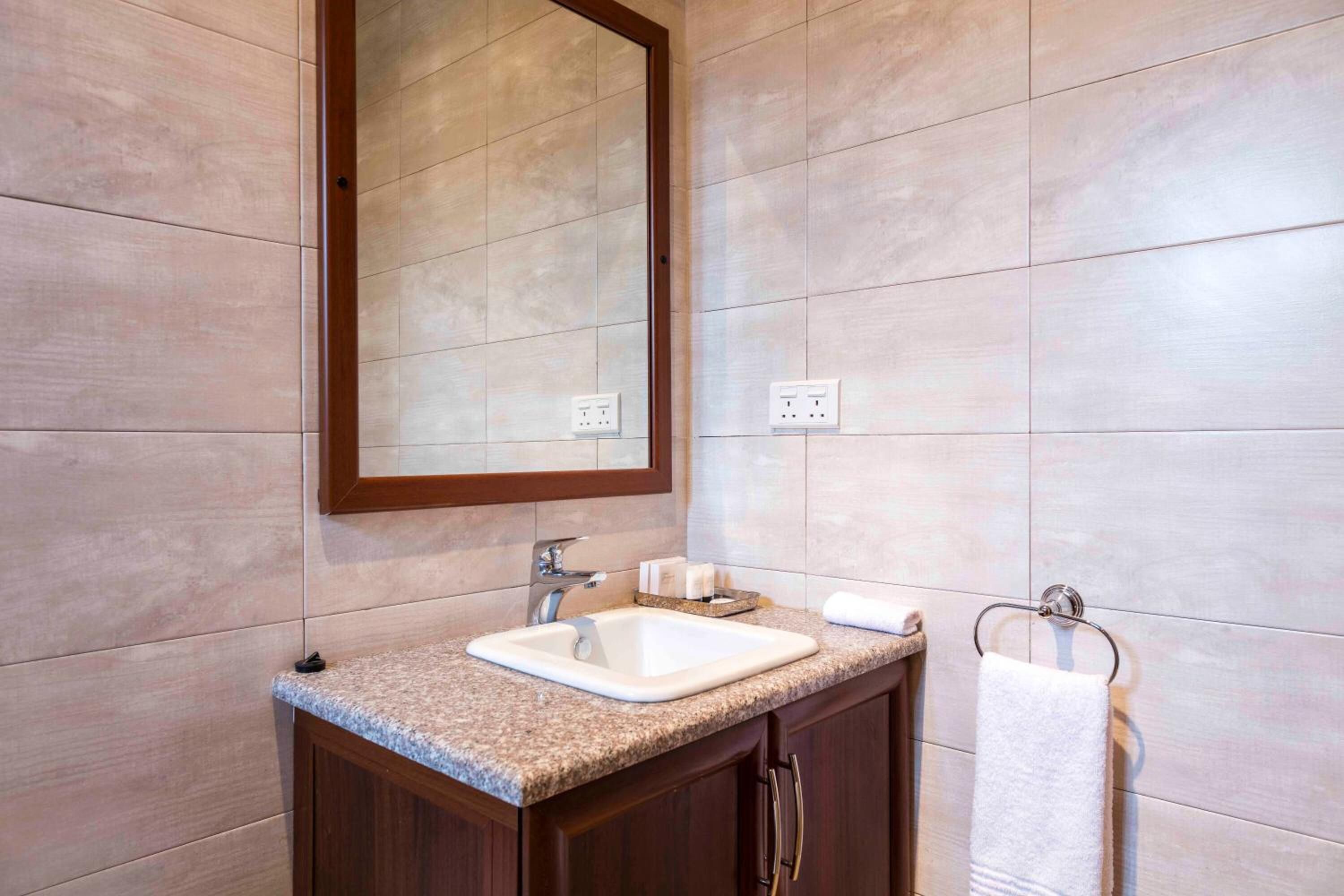 A bathroom with a granite countertop sink, a mirror, and a towel rack.