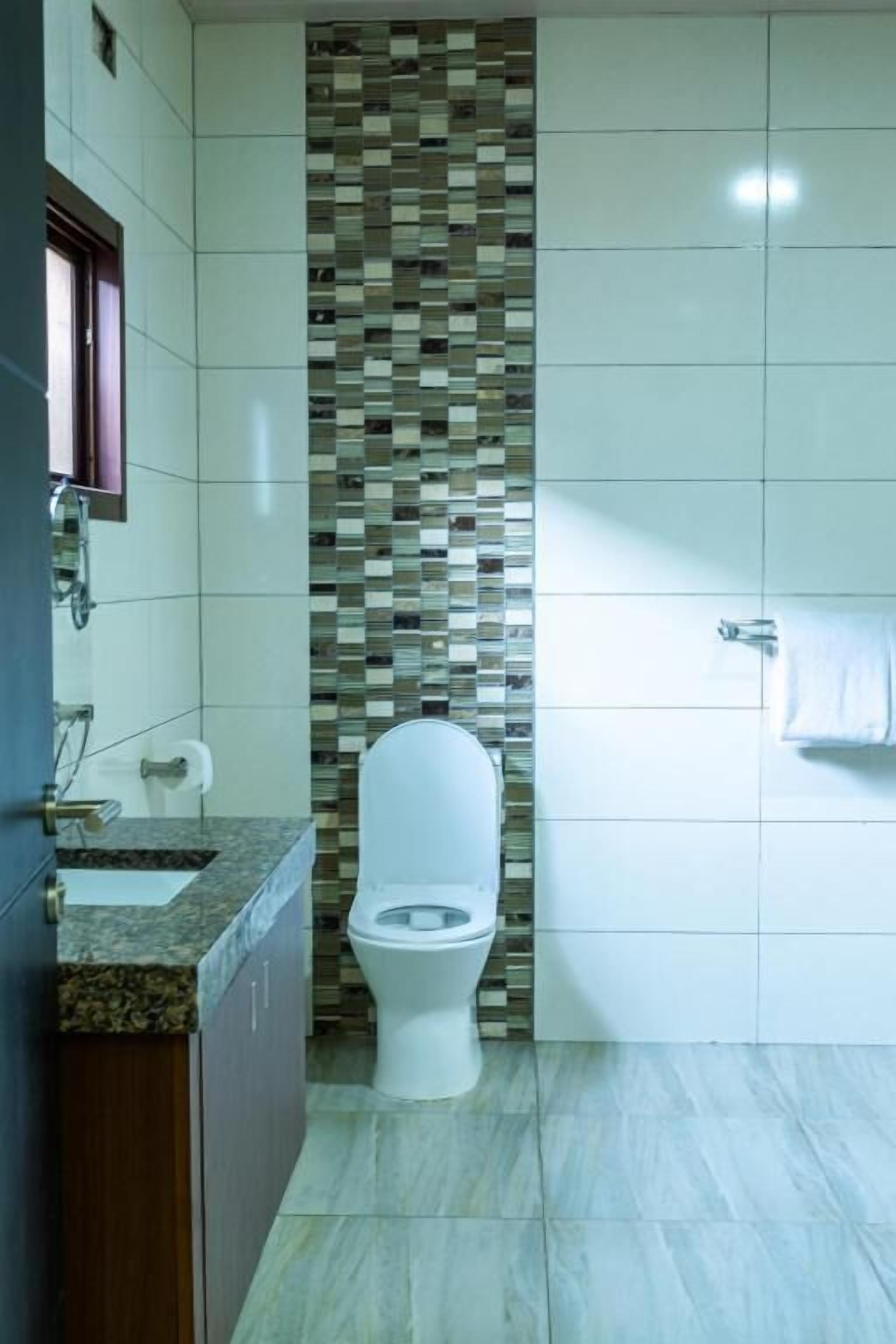 A bathroom with a tiled floor, a toilet, a sink, and a towel rack.