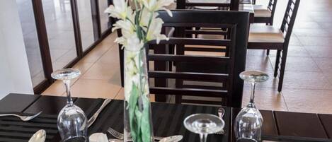 A restaurant with tables set for dining, featuring black striped placemats, silverware, and a vase with white flowers.