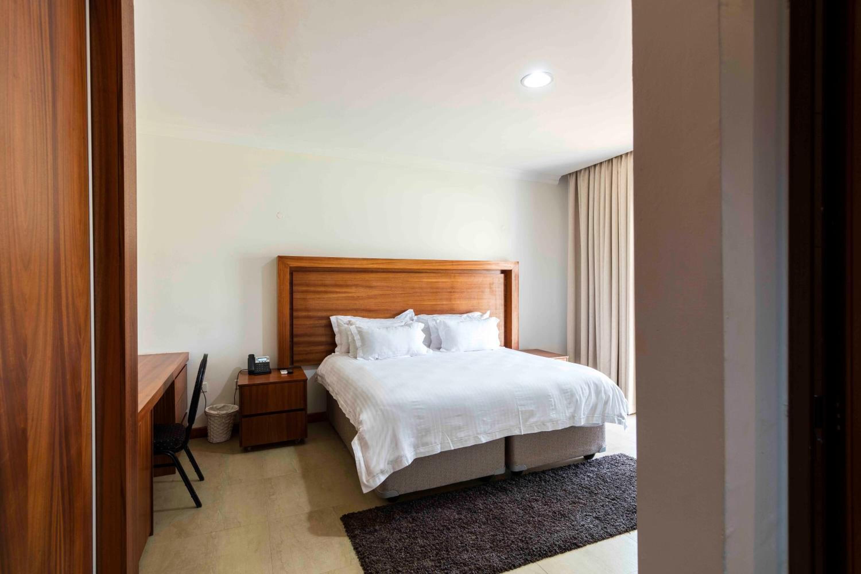 Una habitación de hotel ordenada con una cama de madera, un escritorio y una silla.
