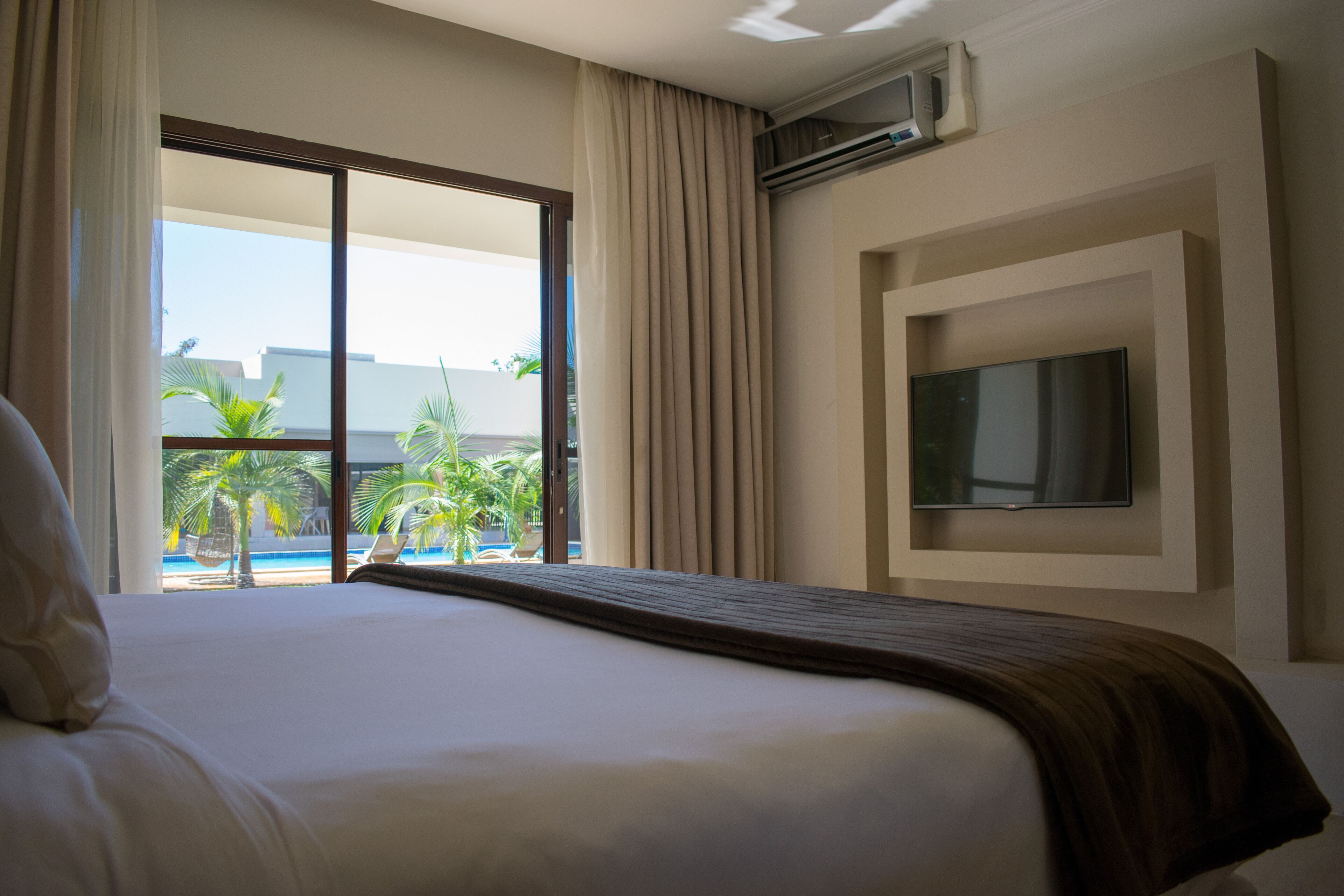 Camera d'albergo con un grande letto, una TV a parete e vista su piscina e palme.