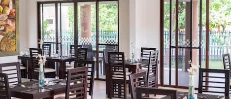 A dining area with multiple tables and chairs, large windows, and a view of greenery outside.