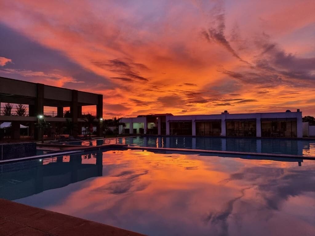 A swimming pool with a sunset sky reflected on the water, surrounded by buildings.
