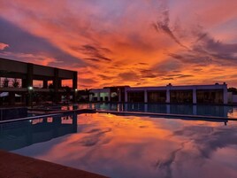 A swimming pool with a sunset sky reflected on the water, surrounded by buildings.