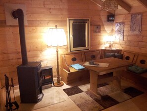 A cozy cabin interior with a wooden sofa, a table, a lamp, and a wood-burning stove.