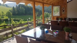A wooden deck with wicker furniture, a table with cards and cups, and a view of a green landscape.