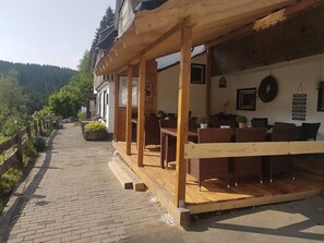 Een houten terras met rieten meubilair, een pad van bakstenen en uitzicht op een beboste helling.