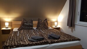 Een opgemaakt bed met gestreepte kussens en een deken, twee bedlampjes en een raam met gordijnen.