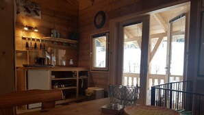 A wooden interior with a kitchen area, a dining table, and a view through a door.