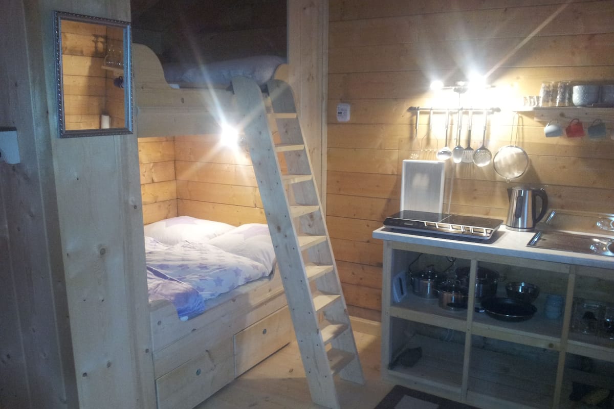 Une petite cabane en bois comprenant un lit superposé, un coin cuisine et une petite salle de bain.