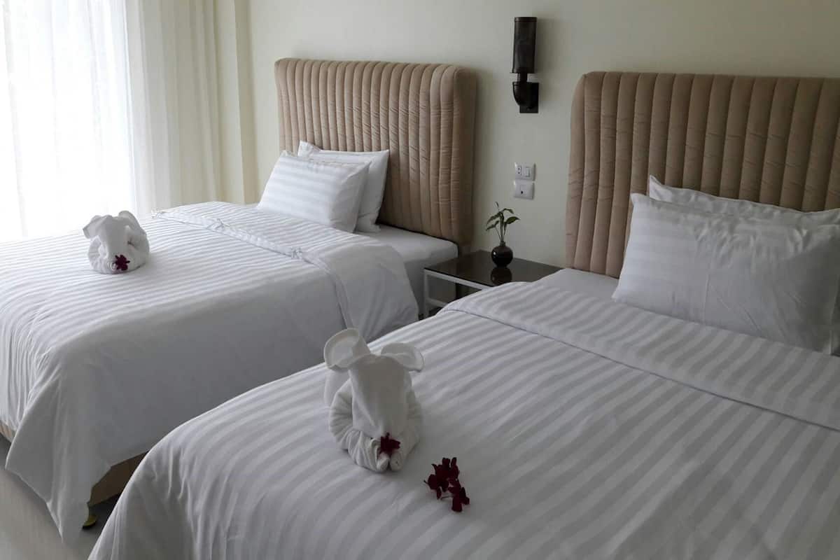 Two beds with white linens, a beige headboard, and a small bedside table with a vase.
