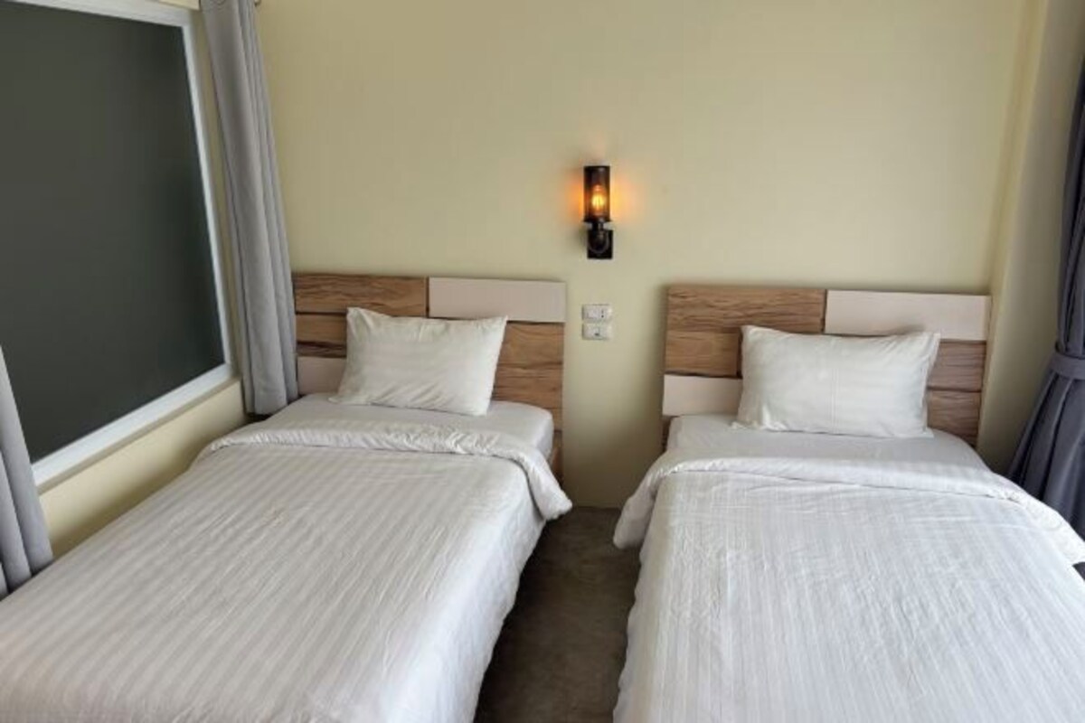 A hotel room with two beds, a nightstand, a wall-mounted lamp, and a window with curtains.