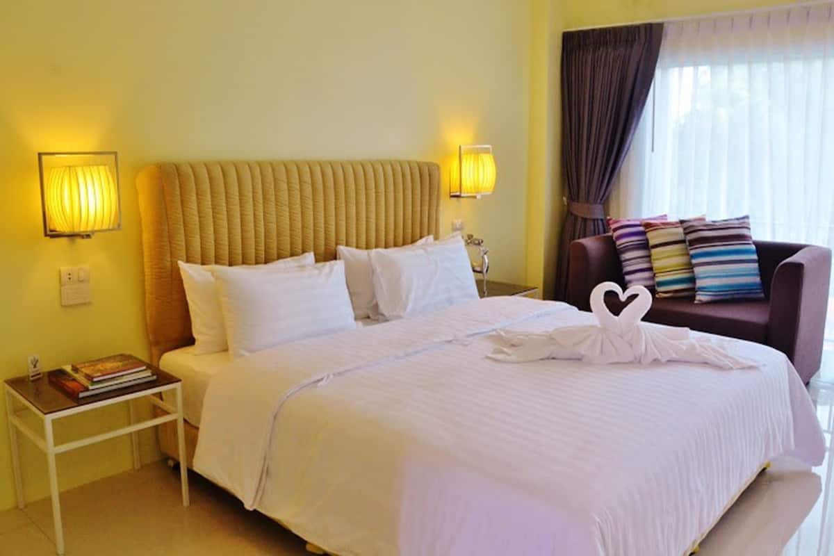A hotel room with a large bed, two bedside tables, a nightstand, a sofa, and a window with curtains.