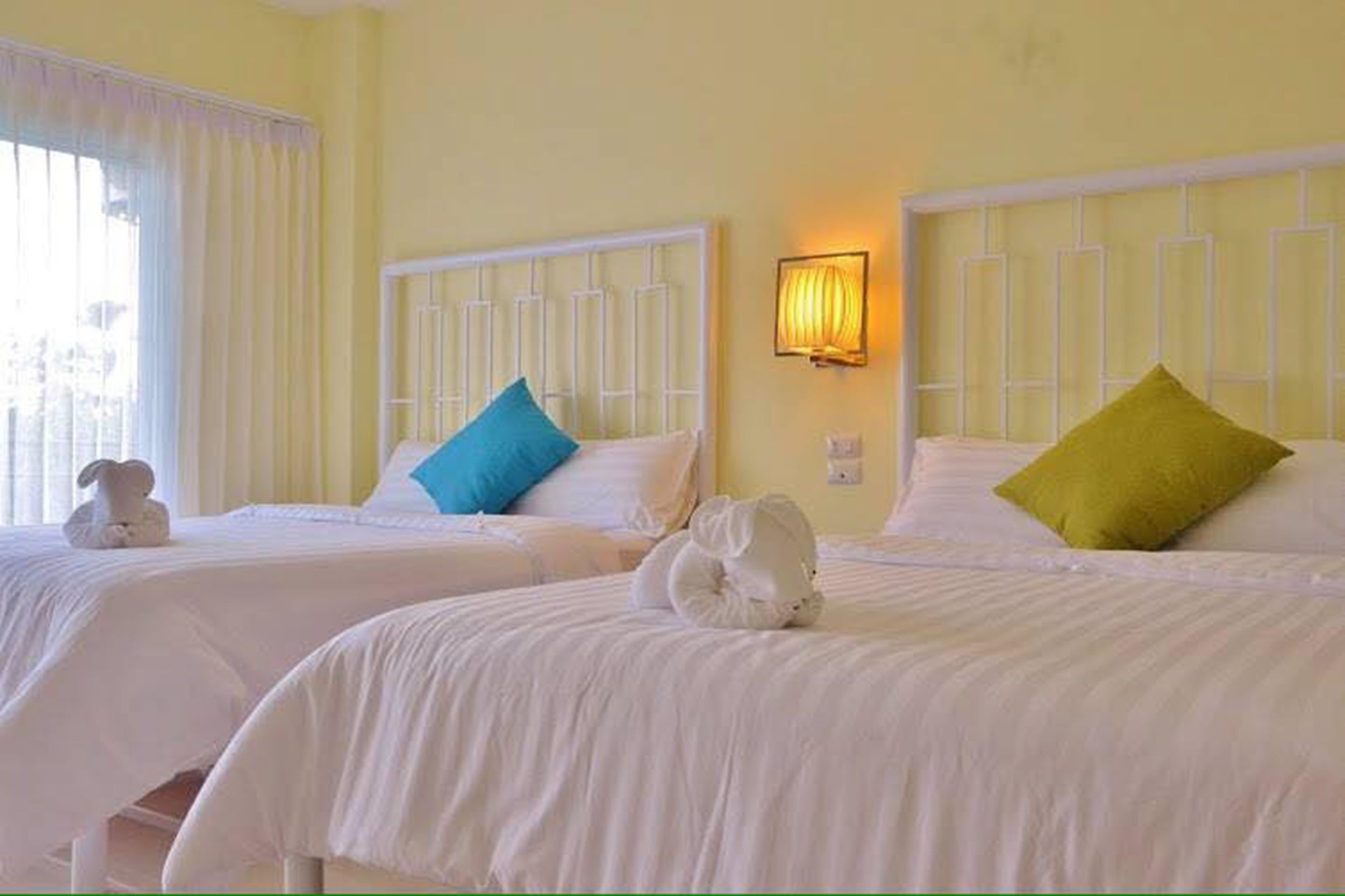 Habitación de hotel con dos camas, cada una con ropa blanca y cabeceras. Hay un aplique de pared sobre las camas y una ventana con cortinas a la izquierda.