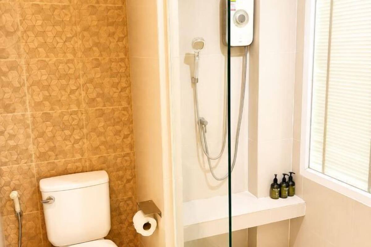 A bathroom with a toilet, shower, and a shelf with toiletries.
