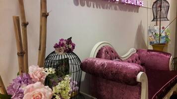 A plush purple sofa, a black birdcage with flowers, and a neon sign reading "SOUTHGATE RESIDENCE".